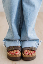 Person wearing blue jeans and brown sandals with a wooden sole on a light background