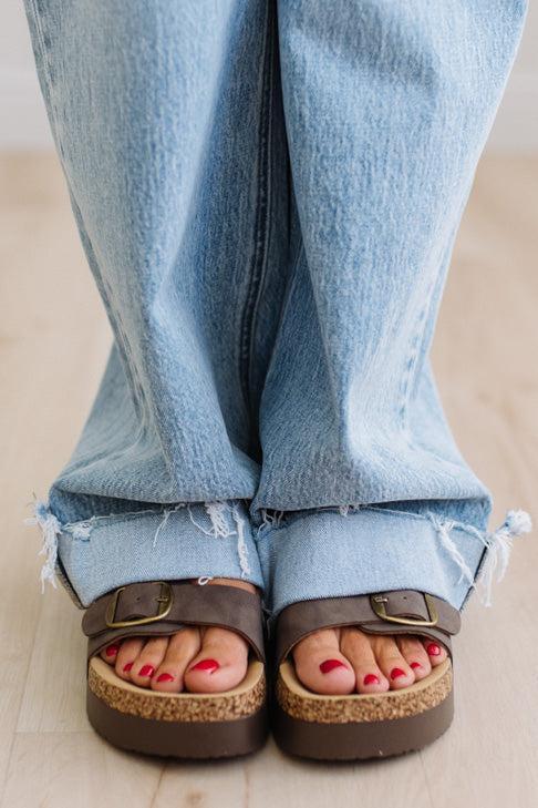 Person wearing blue jeans and brown sandals with a wooden sole on a light background