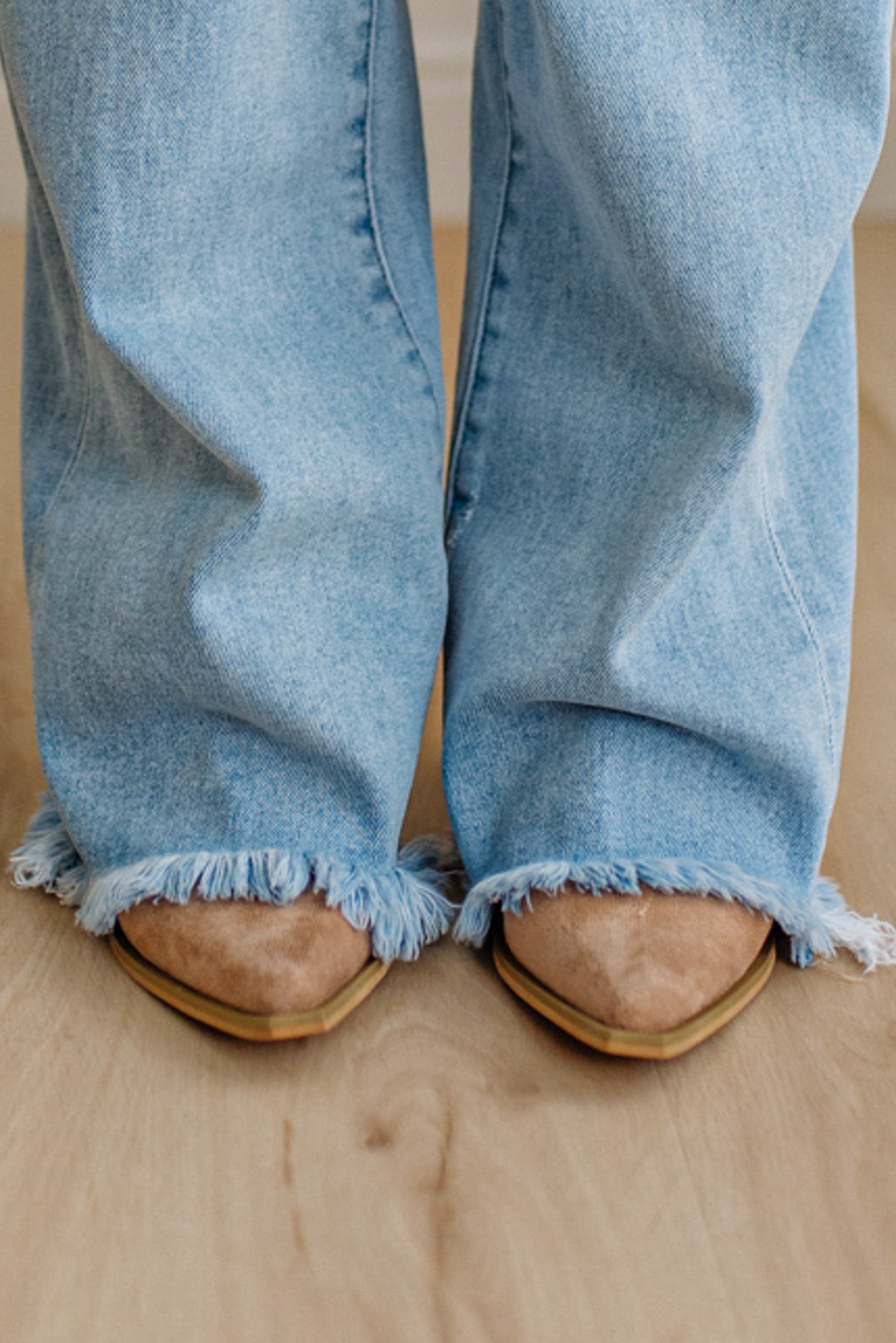 Light blue jeans with frayed hems worn by a person on a wooden floor.