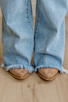 Light blue jeans with frayed hems worn by a person on a wooden floor.