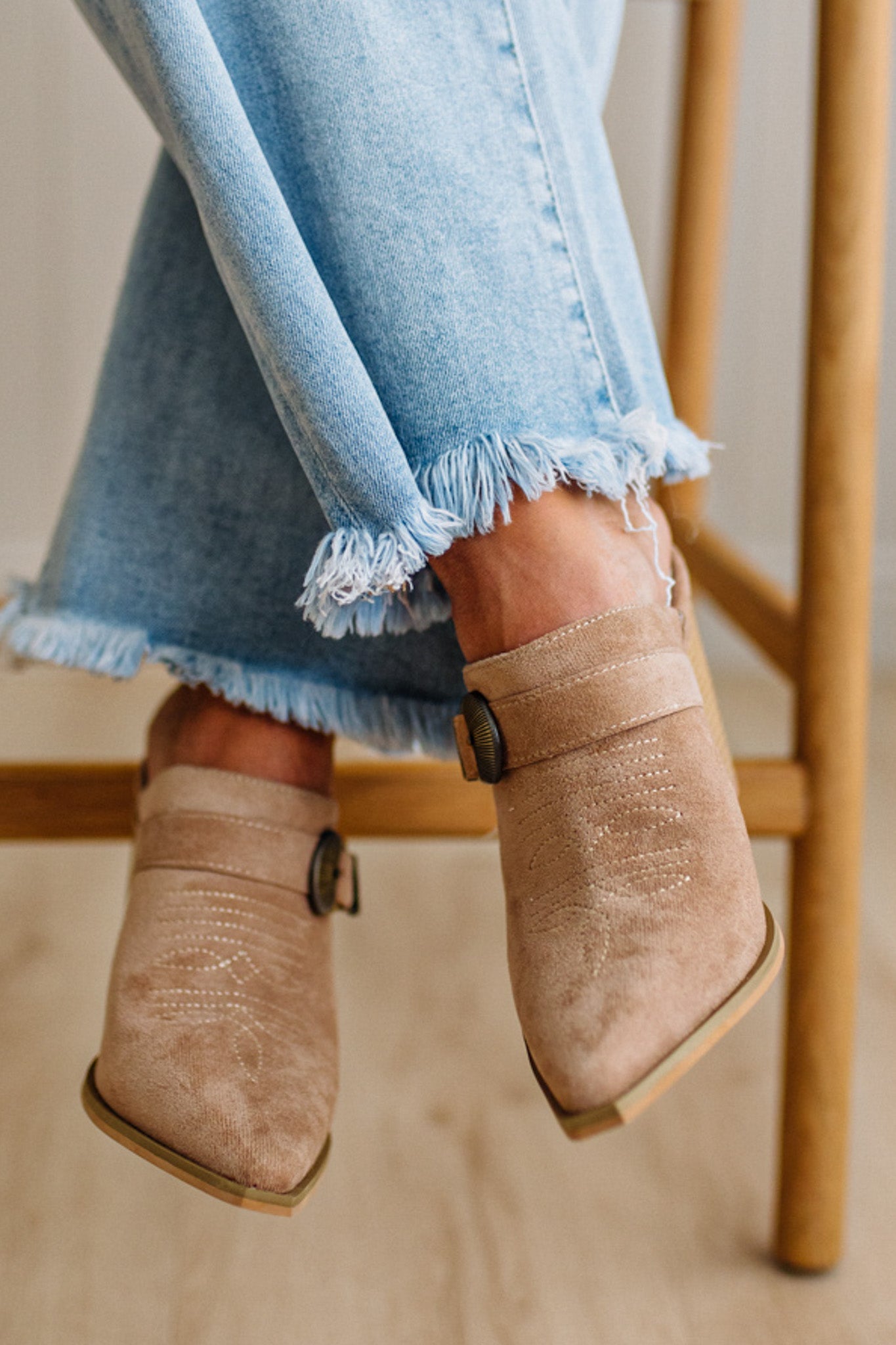 Person wearing beige suede ankle boots with light blue denim jeans.