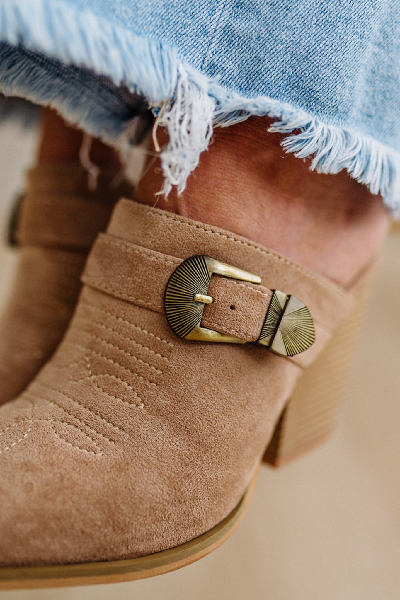 Close-up of brown suede boot with gold buckle detail, worn with denim shorts.