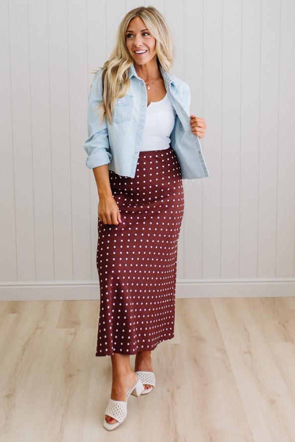 Woman wearing a light blue denim jacket, white top, and maroon polka dot skirt indoors.