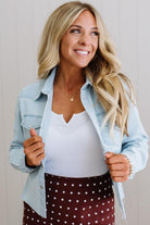 Woman wearing a light blue denim jacket over a white top and polka dot skirt, smiling.