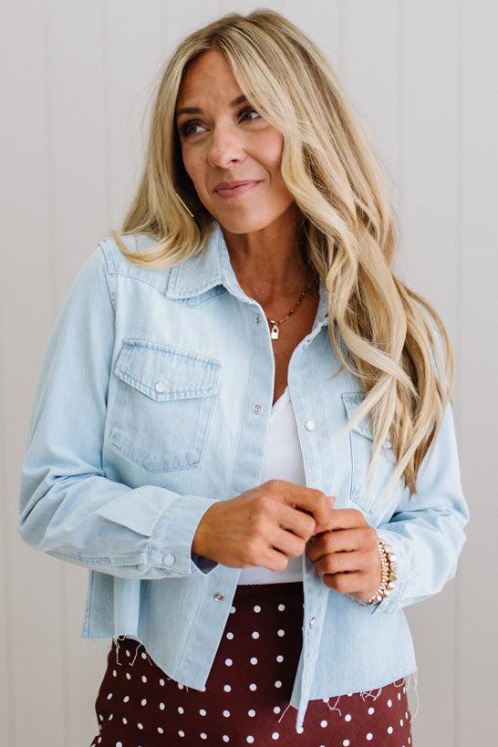 Woman wearing a light blue denim jacket over a white shirt with a polka dot skirt.