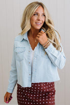 Woman wearing a light blue denim jacket over a white top and maroon skirt with white polka dots.