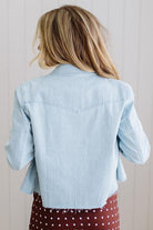 Person wearing a light blue denim jacket over a red polka dot dress against a plain background
