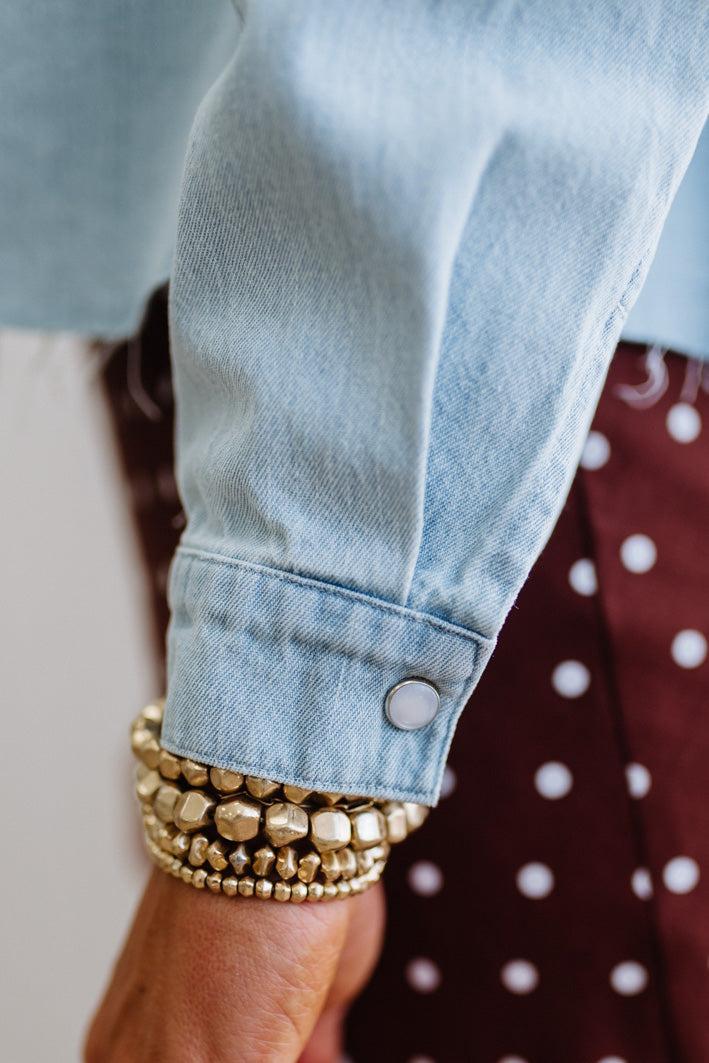 Close-up of a person wearing a light blue denim jacket with rolled-up sleeves and gold bracelets.