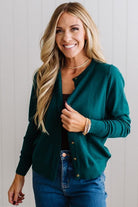 Blonde woman in dark jeans modeling in bright studio wearing a solid green cardigan with brown button front.