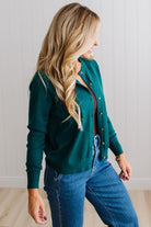 Blonde woman in dark jeans modeling in bright studio wearing a solid green cardigan with brown button front.