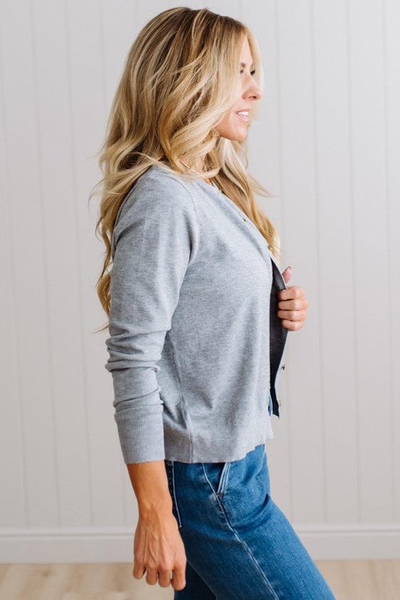 Blonde woman in dark jeans modeling in bright studio wearing a heather grey cardigan with brown button front.