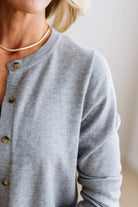 Blonde woman in dark jeans modeling in bright studio wearing a heather grey cardigan with brown button front.