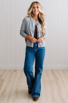 Blonde woman in dark jeans modeling in bright studio wearing a heather grey cardigan with brown button front.