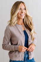 Blonde woman in dark jeans modeling in bright studio wearing a heather mocha cardigan with brown button front.