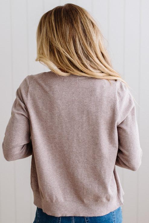 Blonde woman in dark jeans modeling in bright studio wearing a heather mocha cardigan with brown button front.