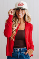 Blonde woman in dark jeans modeling in bright studio wearing a red cardigan with brown button front.