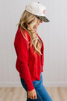 Blonde woman in dark jeans modeling in bright studio wearing a red cardigan with brown button front.