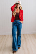 Blonde woman in dark jeans modeling in bright studio wearing a red cardigan with brown button front.