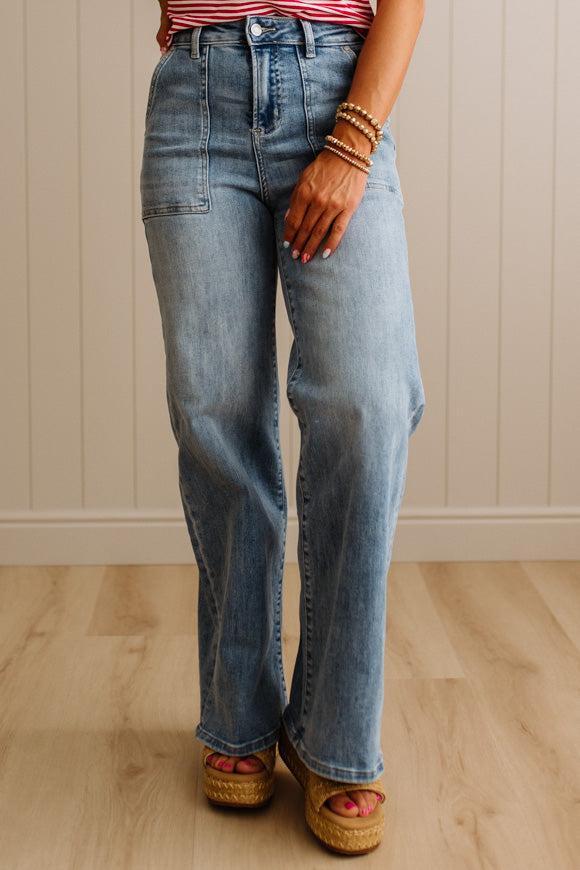 Person wearing blue jeans and sandals standing on a wooden floor with a neutral wall background
