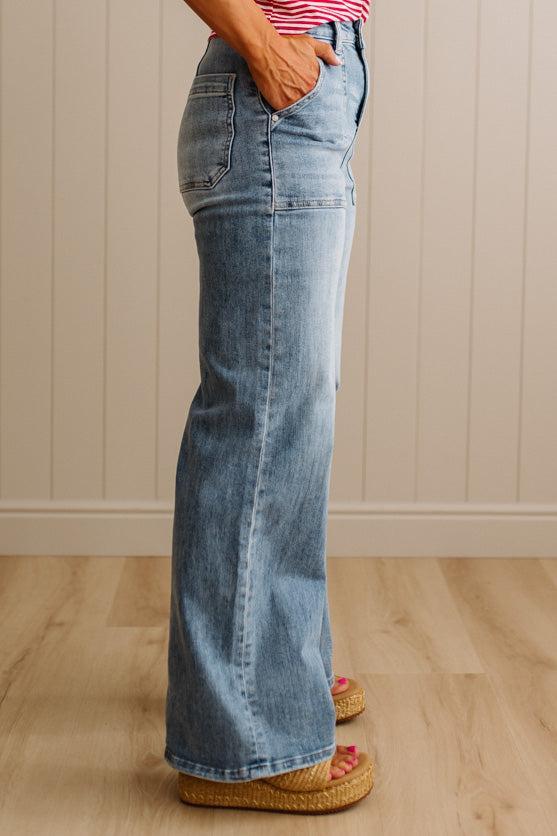 Person wearing blue flared jeans standing on a wooden floor with a neutral wall background
