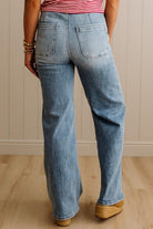 Person wearing blue jeans and a striped shirt against a neutral wall.