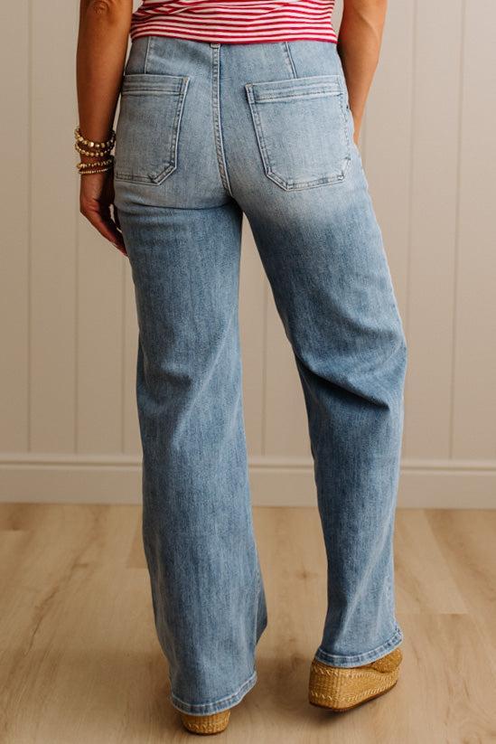 Person wearing blue jeans and a striped shirt against a neutral wall.