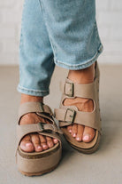 Beige sandals worn with rolled-up blue jeans on a neutral background