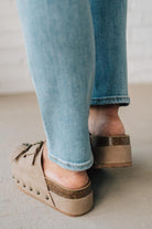 Person wearing blue jeans and brown platform sandals on a neutral background