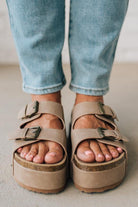 Beige sandals with buckles worn with light blue jeans on a neutral background