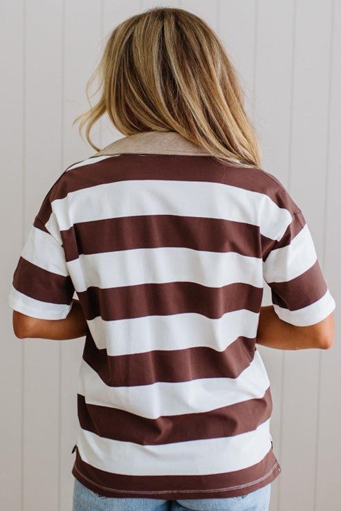 Person wearing a brown and white striped shirt against a light wooden panel background