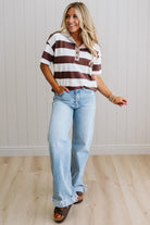 Woman wearing a striped shirt and jeans standing against a light wooden paneled wall.