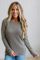 A woman modeling a long-sleeve striped knit top and blue jeans in a bright room with white paneled walls and light wood flooring.
