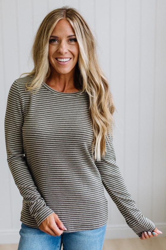 A woman modeling a long-sleeve striped knit top and blue jeans in a bright room with white paneled walls and light wood flooring.