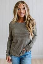 A woman modeling a long-sleeve striped knit top and blue jeans in a bright room with white paneled walls and light wood flooring.