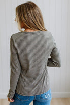 A woman shown from the back wearing a long-sleeve shirt with thin horizontal gray and white stripes, paired with blue jeans, against a white paneled wall.