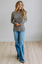 A woman modeling a long-sleeve striped knit top and blue jeans in a bright room with white paneled walls and light wood flooring.