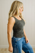 Woman wearing a green tank top and blue jeans against a neutral background