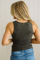 Person wearing a black tank top and blue jeans with a neutral background