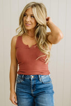 Woman wearing a rust-colored tank top and blue jeans against a neutral background