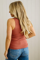 Woman wearing a rust-colored tank top and blue jeans against a white wall.
