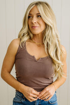 Woman wearing a brown tank top and blue jeans against a neutral background