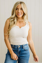 Woman wearing a white tank top and blue jeans against a light wooden panel background
