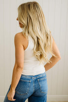 Woman wearing a white tank top and blue jeans against a neutral background