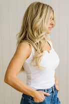 Woman wearing a white tank top and blue jeans against a neutral background