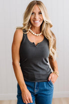 Woman wearing a charcoal grey tank top and blue jeans against a neutral background