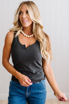 Woman wearing a charcoal grey tank top and blue jeans against a neutral background