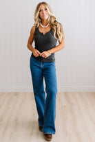 Woman wearing a charcoal grey tank top and blue jeans against a neutral background