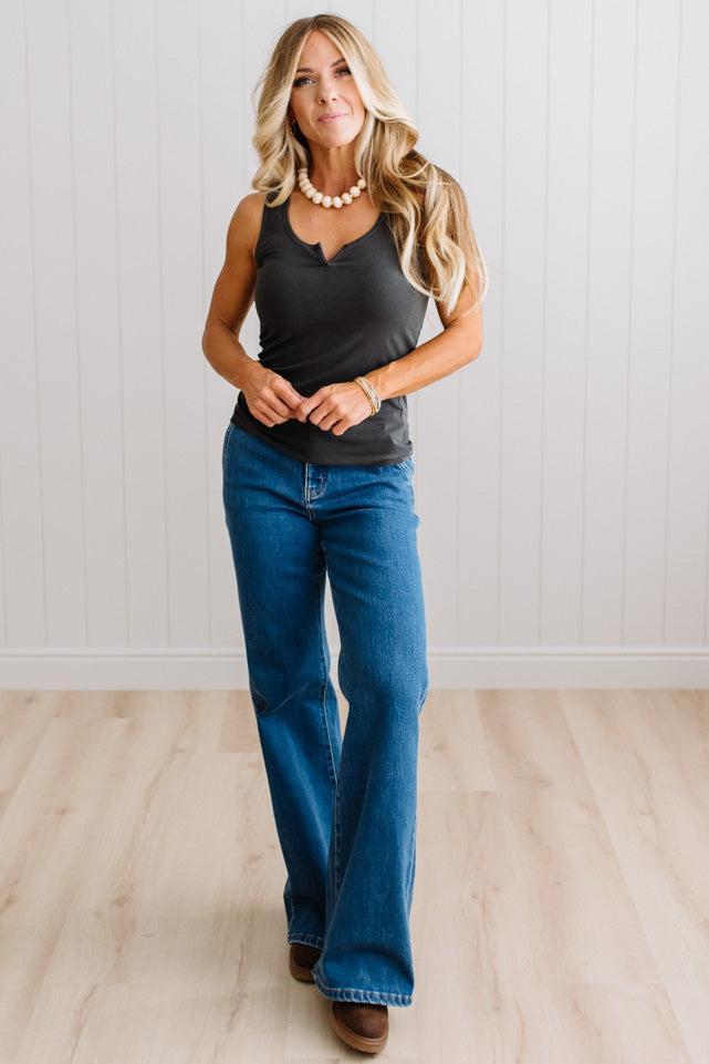 Woman wearing a charcoal grey tank top and blue jeans against a neutral background