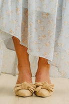 Person wearing beige flat shoes with bow details and a light floral dress.