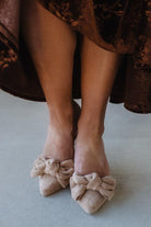 Beige shoes with bow details worn by a person in a brown dress.